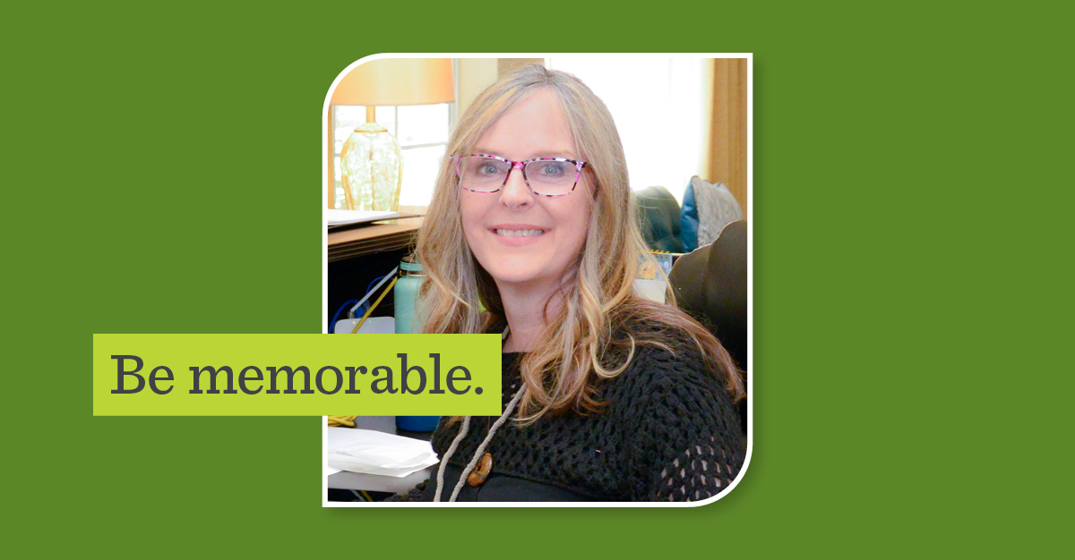 photograph of woman smiling at her desk in a black top with a name tag on. Overlay text on image reads "be empowered"