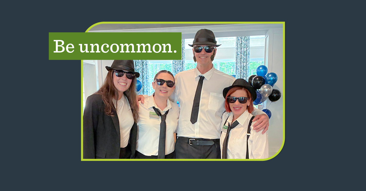 A group of people dressed as the Blues Brothers with a green banner overlay that says "Be uncommon."