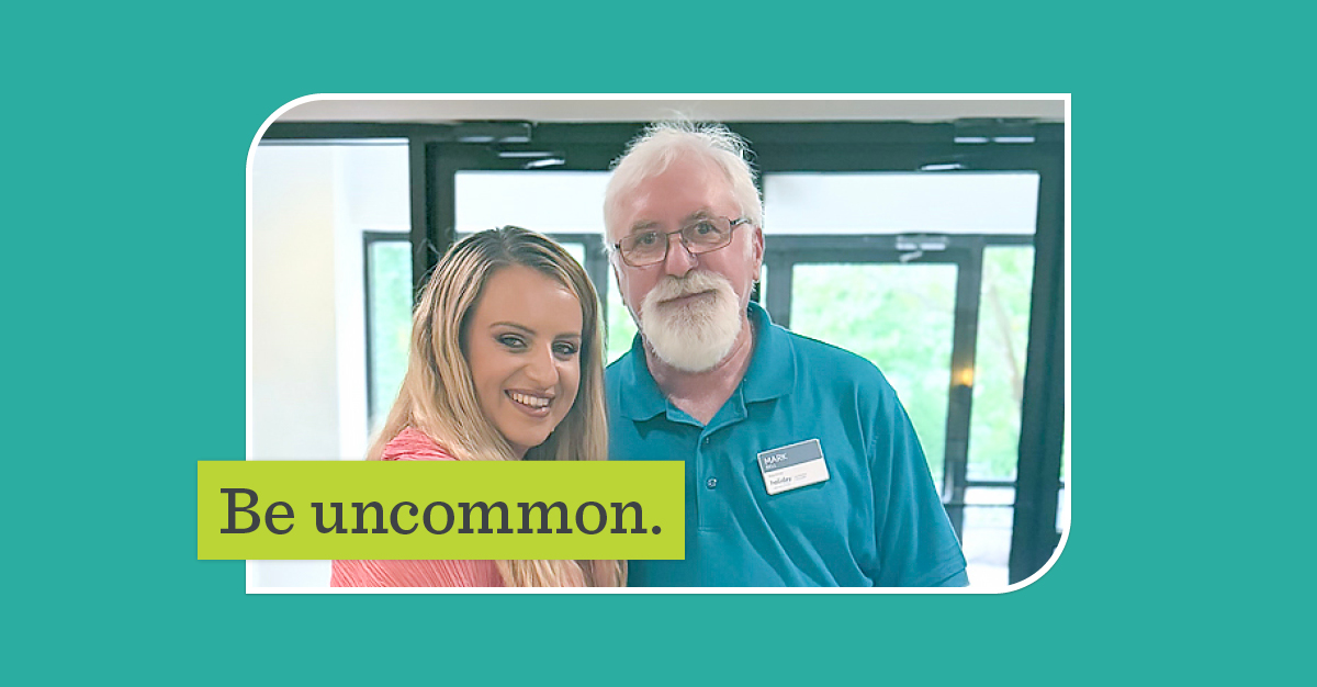 Mark Bell posing with a resident. A green overlay says, "Be uncommon".